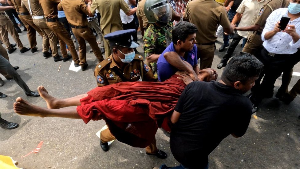 A Sri Lankan monk is carried by police officers past a line of police officers in front of crowds