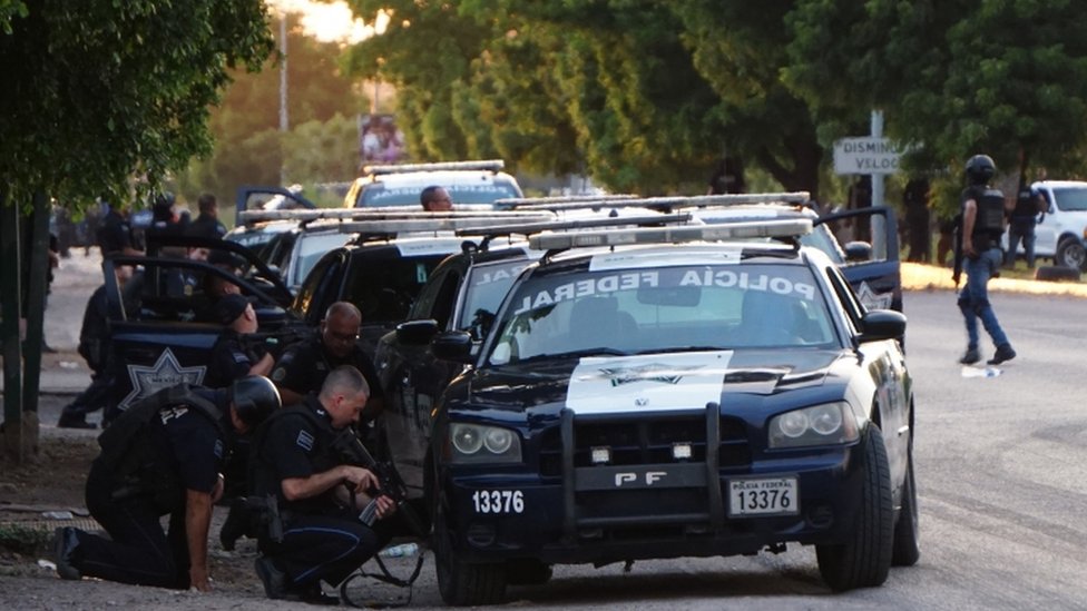 Мексиканская полиция укрывается за автомобилем во время перестрелки с членами картеля
