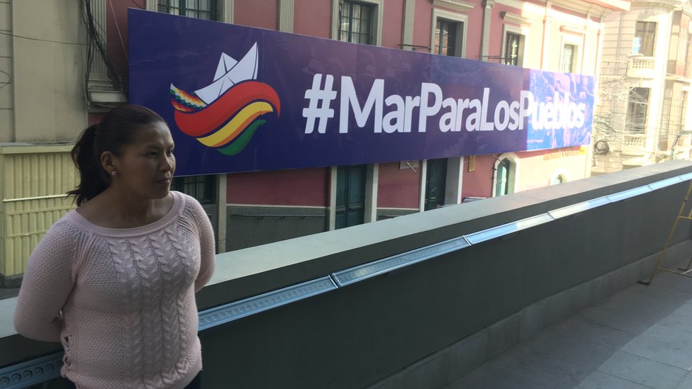 Mujer al lado de valla que dice #MarParaLosPueblos