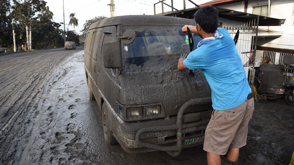 Житель очищает машину от грязи и золы