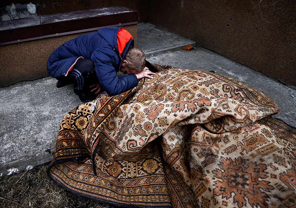 رجل يبكي قرب جثة صديقه مغطى ببساط مزخرف قتل بحسب السكان برصاص جنود روس في أوكرانيا.