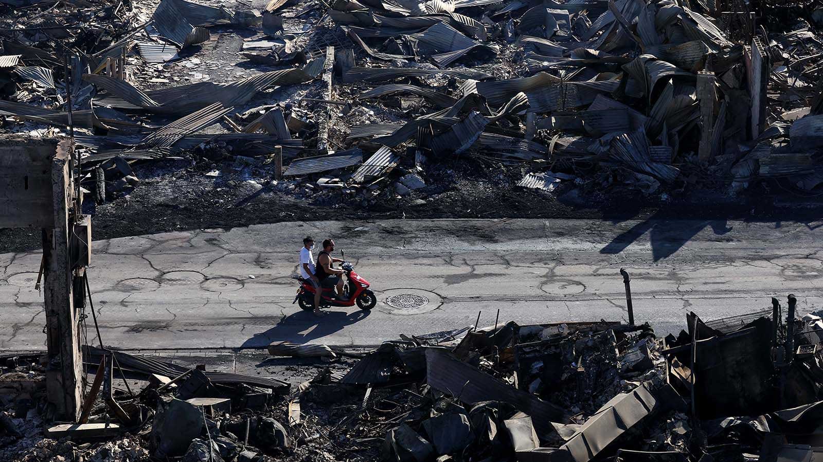 Aerial view of two men riding a scooter though a street destroyed by a wildfire in Lahaina, Hawaii - 11 August, 2023.