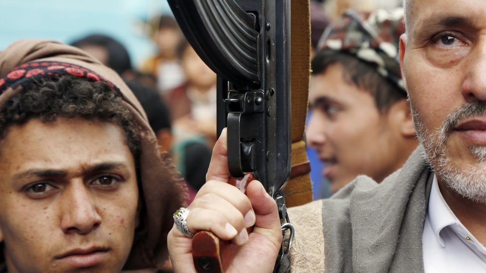 رجل يحمل السلاح برفق شاب خلال تظاهرة في إحدى المناطق الخاضعة لسيطرة جماعة أنصار الله الحوثية في اليمن