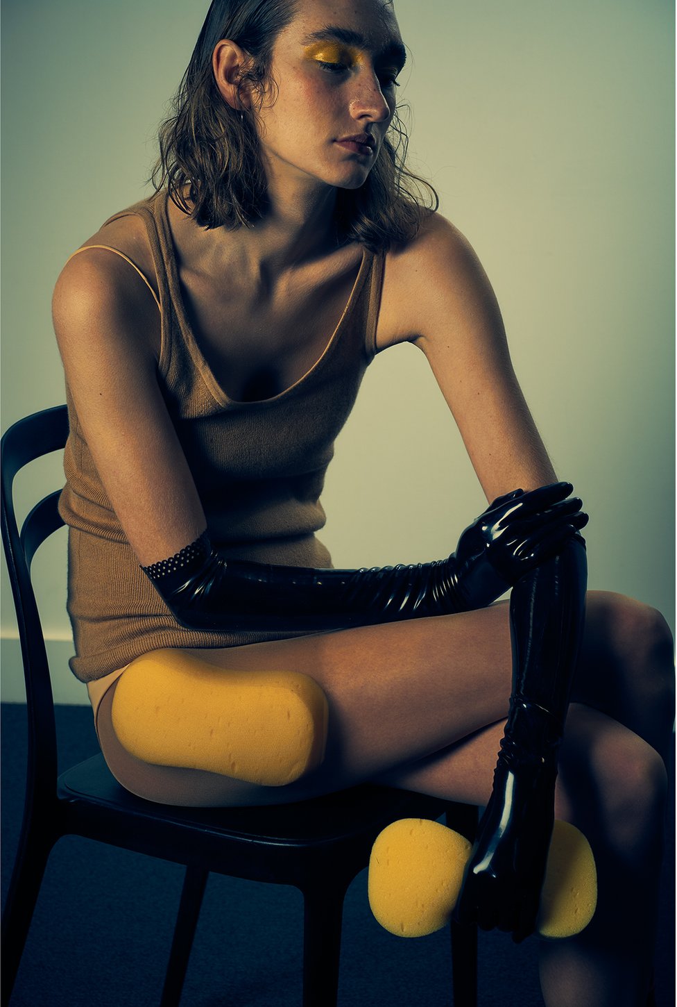 A model sits on a chair with a sponge clutched in her hand and one attached to her thigh