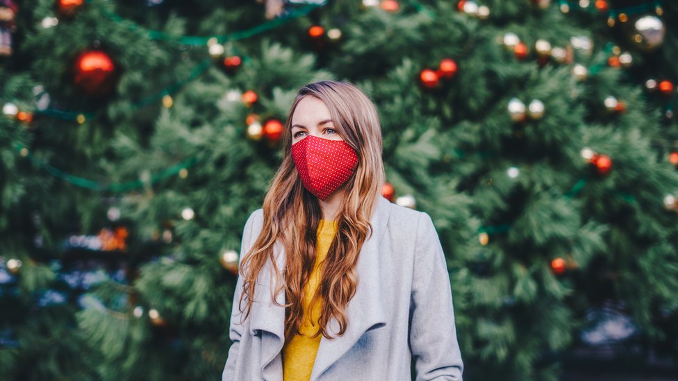 Mujer con mascarilla frente al árbol de Navidad