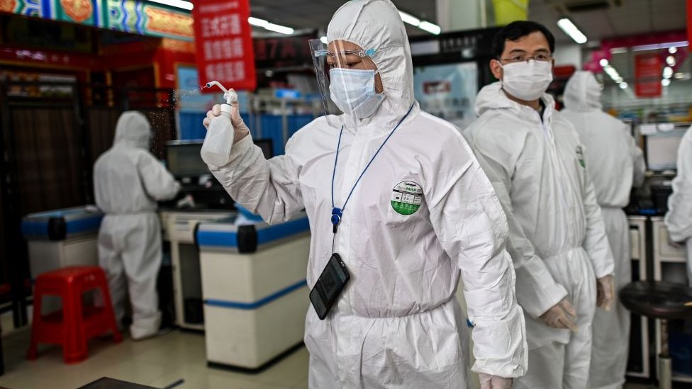 A woman wearing a protective suit sprays disinfectant in a pharmacy in Wuhan, in China‘s central Hubei province on March 30, 2020