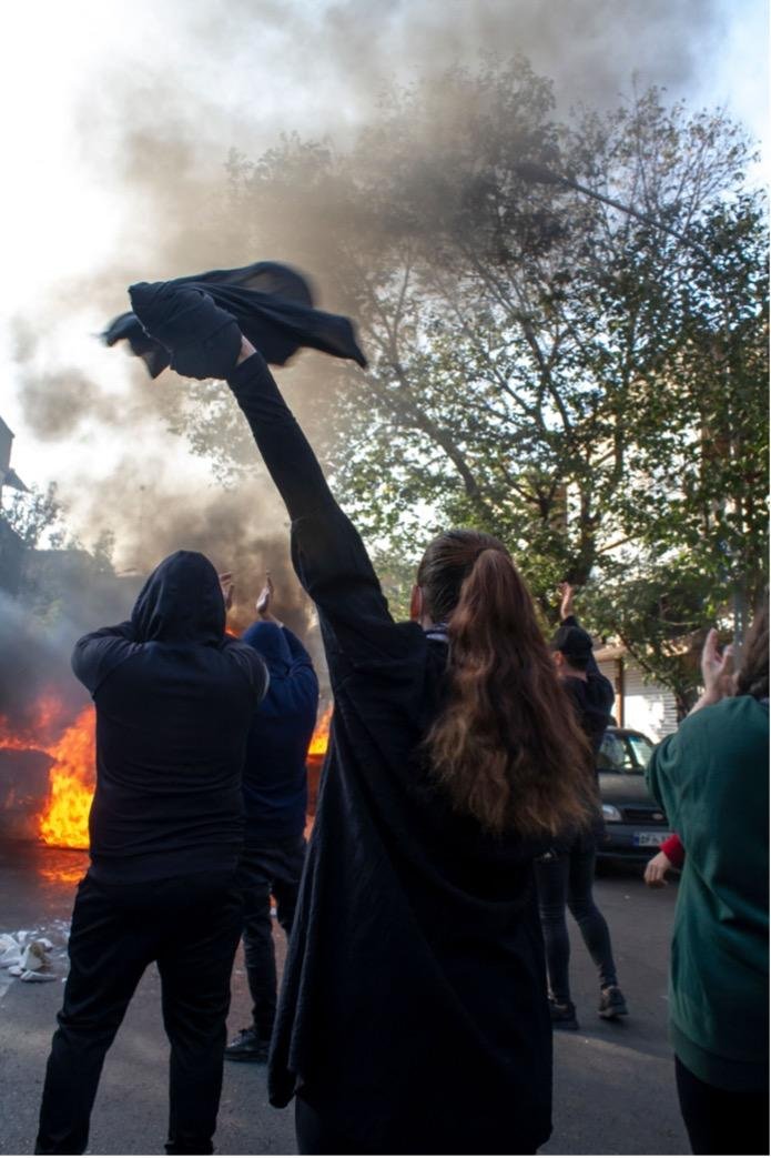 A woman without wearing a hijab beside other protesters gathers around burning dumpsters during a protest. The nationwide protests started after the death of Mahsa Amini, a 22-year-old girl who died under the custody of the Islamic Republic's Morality Police on September 16th, 2022 in Tehran, Iran.