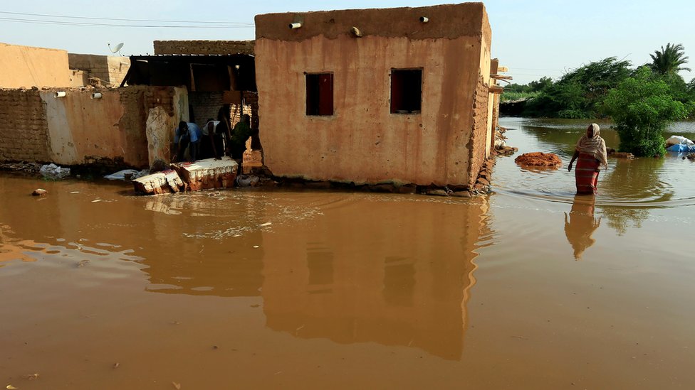 Residents walk through floodwaters from the Blue Nile as it submerges their neighborhood in the Al-Ikmayr area of Omdurman in Khartoum