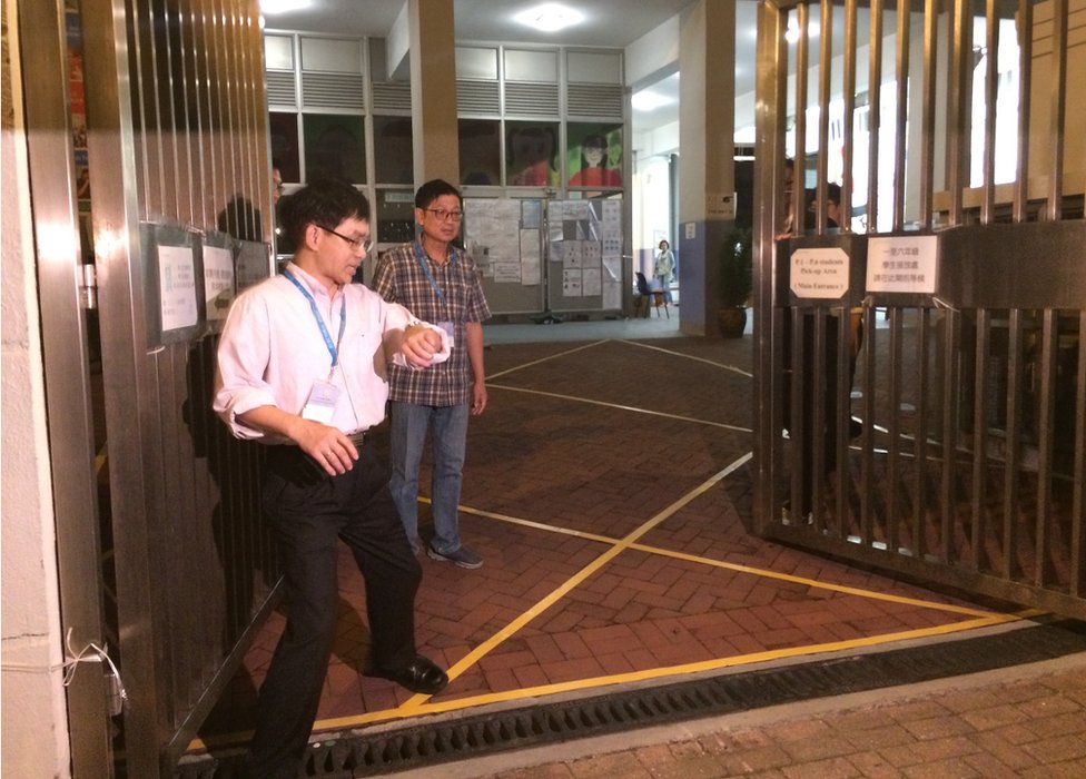 Фотография сотрудников избирательных комиссий, закрывающих ворота в Гонконге 22 ноября 2015 г.