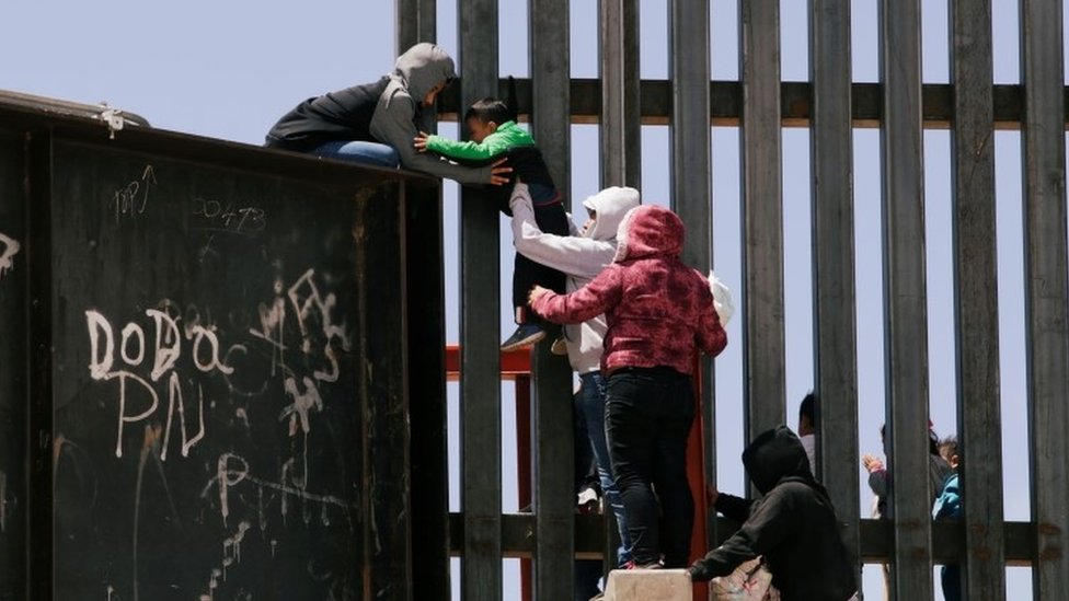 Маленького мальчика передают через пограничную стену в США.