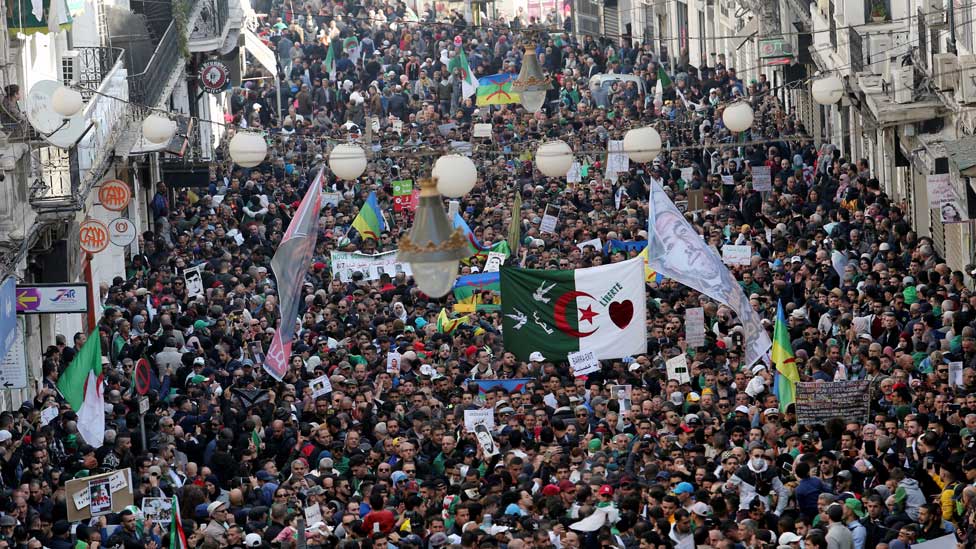Алжирцы несут транспаранты и флаги во время демонстрации в честь первой годовщины протестов, свергнувших президента Абдельазиза Бутефлика, в Алжире, Алжир, 22 февраля 2020 г.