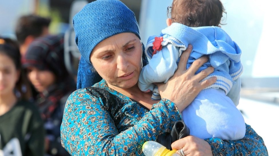 Перемещенная сирийская женщина, спасшаяся от насилия после турецкого наступления в Сирии, несет ребенка