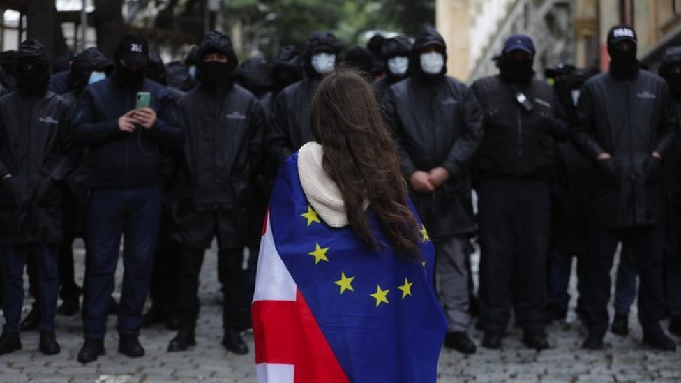 Devojka ogrnuta zastavama gruzije i Evropske unije ispred policije