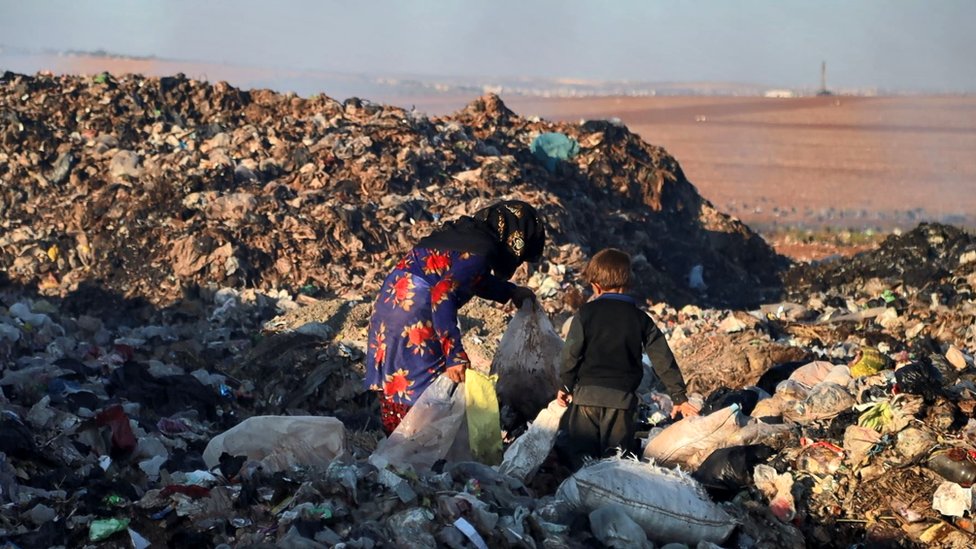 Mujer con un niño revolviendo el basurero