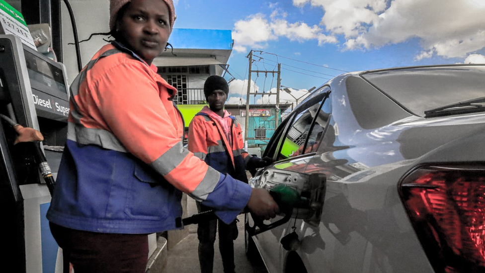 Female pump attendant fills a car at a petrol station in Kenya