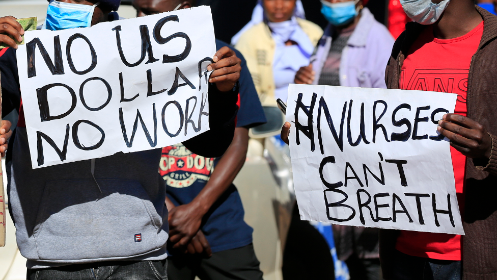 Enfermeros en una manifestación afuera del hospital central de Harare en julio 2020 con letreros que dicen "sin dólares estadounidenses no hay trabajo" y "los enfermeros no pueden respirar"
