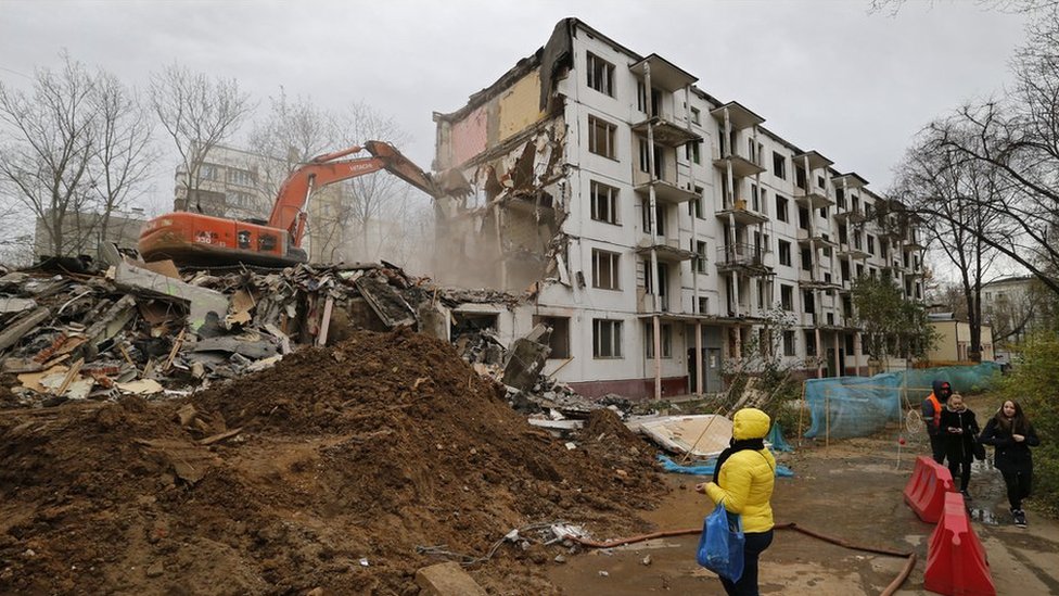 Женщина наблюдает, как экскаватор и рабочие сносят пятиэтажное здание «Хрущевки» в Москве