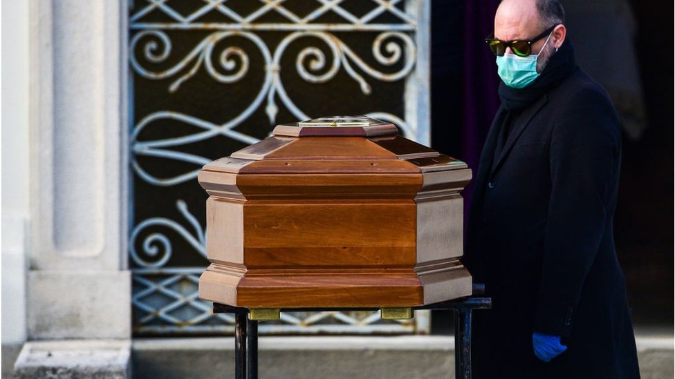 A man wearing a face mask stands by the coffin of his mother during a funeral service in the closed cemetery of Seriate, near Bergamo, Lombardy, on March 20,