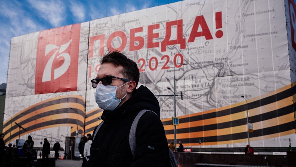 رجل يرتدي قناع وجه، وسط مخاوف من فيروس "كوفيد - 19" التاجي، يمشي أمام لافتة ضخمة بمناسبة الذكرى 75 المقبلة للانتصار على ألمانيا النازية في الحرب العالمية الثانية