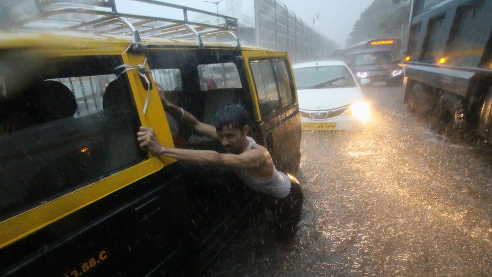 Мужчина толкает такси по заболоченной улице во время проливных дождей в Мумбаи, Индия, 01 июля 2019 года