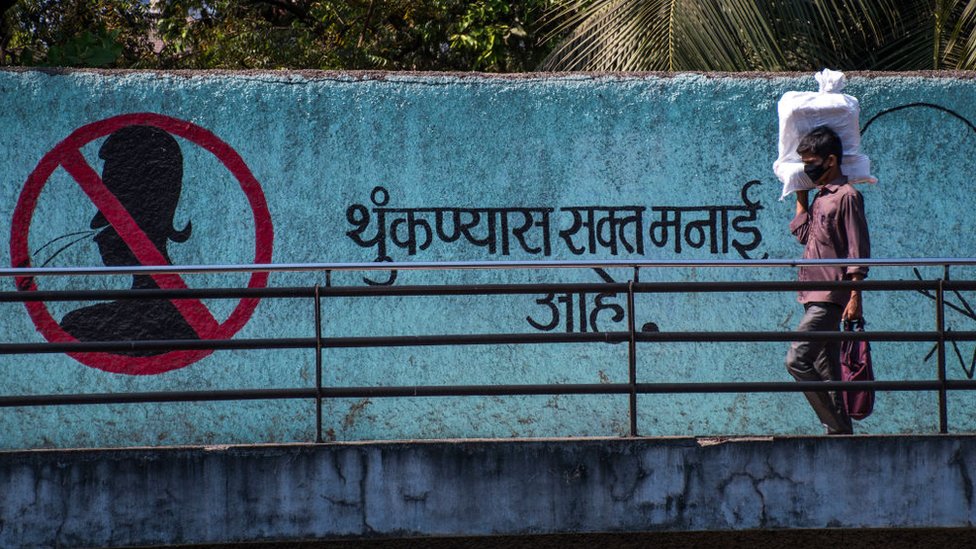 Um homem usa máscara como proteção a próximo a uma mensagem pintada em um muro pedindo para as pessoas não cuspirem. Foto tirada em 18 de março de 2020 em Mumbai, Índia.
