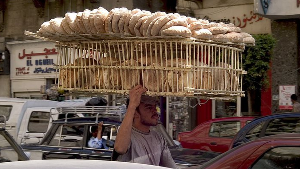 A bread seller carries his product in a Cario street