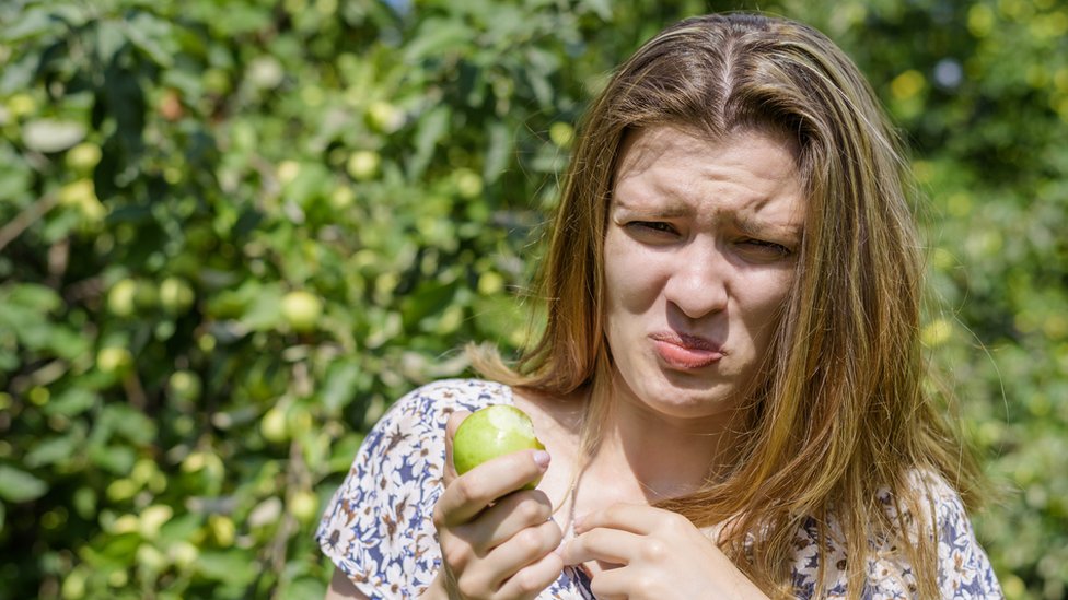 Una mujer asqueada tras comer una manzana.