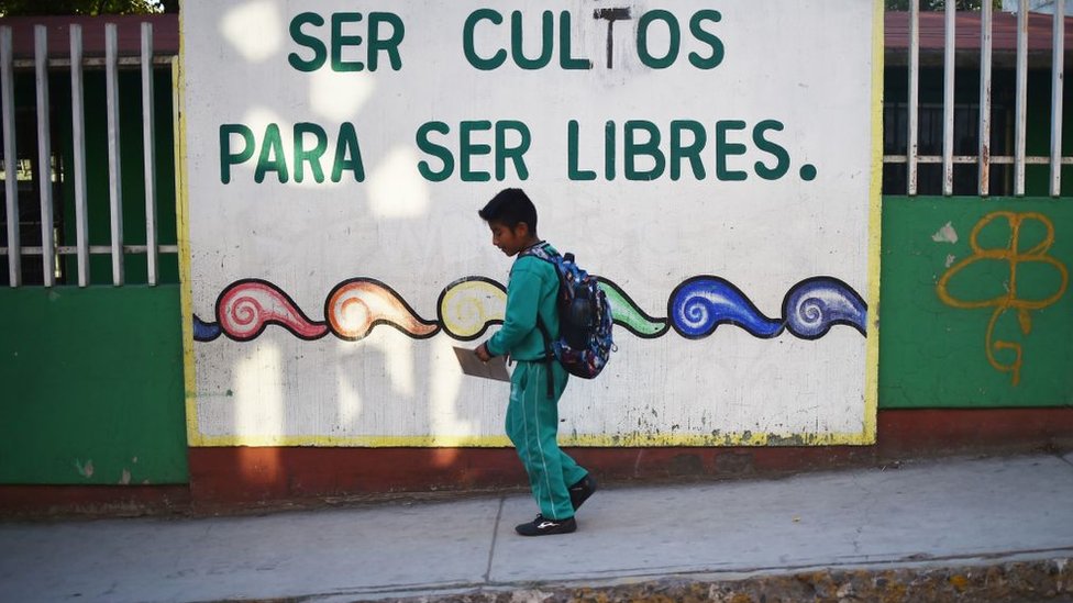 Un niño mexicano camina frente un cartel: "Ser cultos para ser libres".
