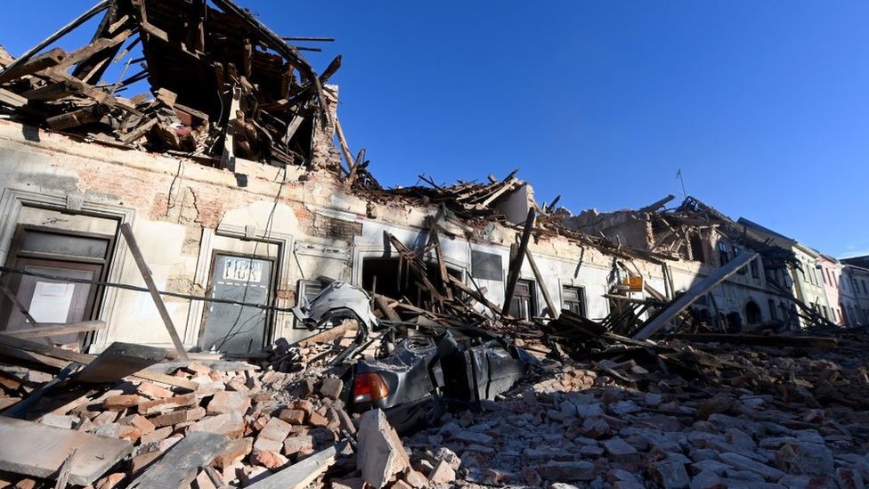 This photograph taken on December 29, 2020, shows the wreckage of a car and damaged buildings in Petrinja