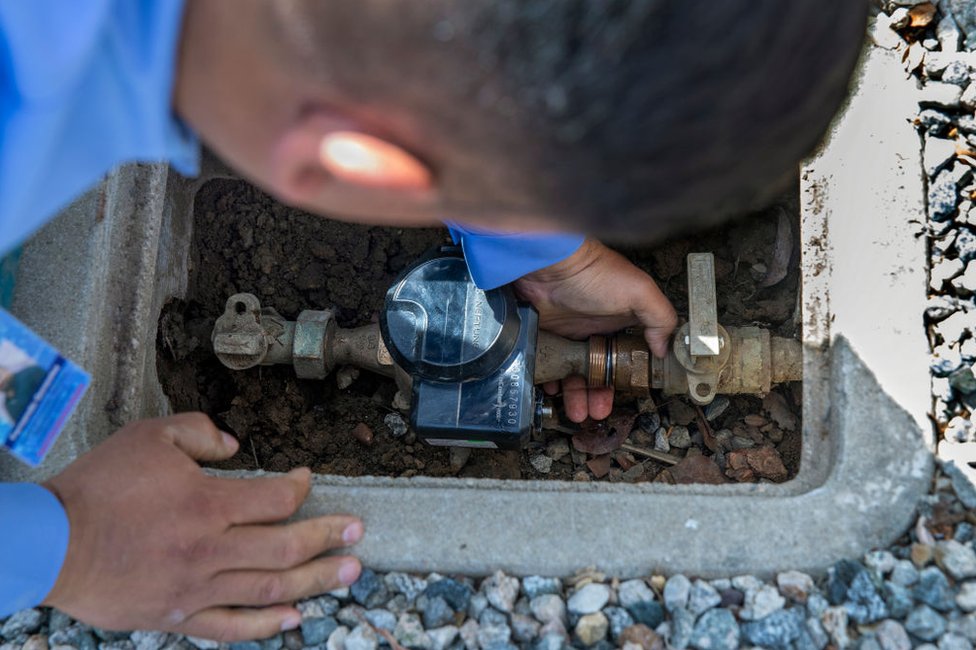 Fernando González, del Distrito Municipal de Agua Las Vírgenes, instala un limitador de flujo en la toma de agua frente a una casa de Calabasas, California, el 2 de junio de 2022.