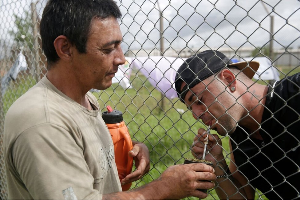 Двое мужчин пьют чай мате через забор в тюрьме Пунта-де-Рьелес