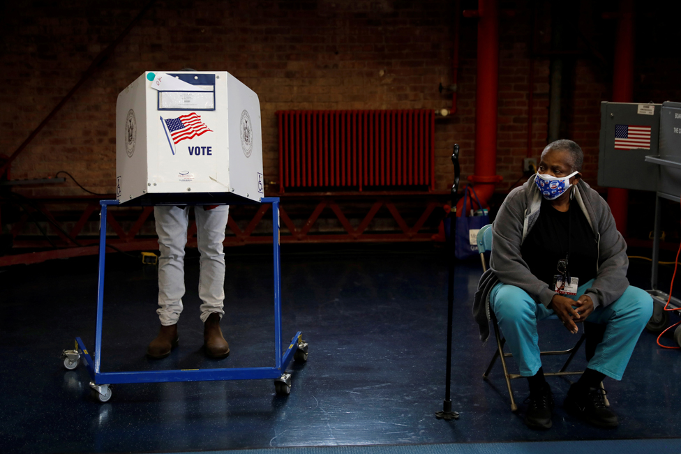 An election volunteer stands by as a voter fills out a ballot in a booth in New York City, 27 October 2020