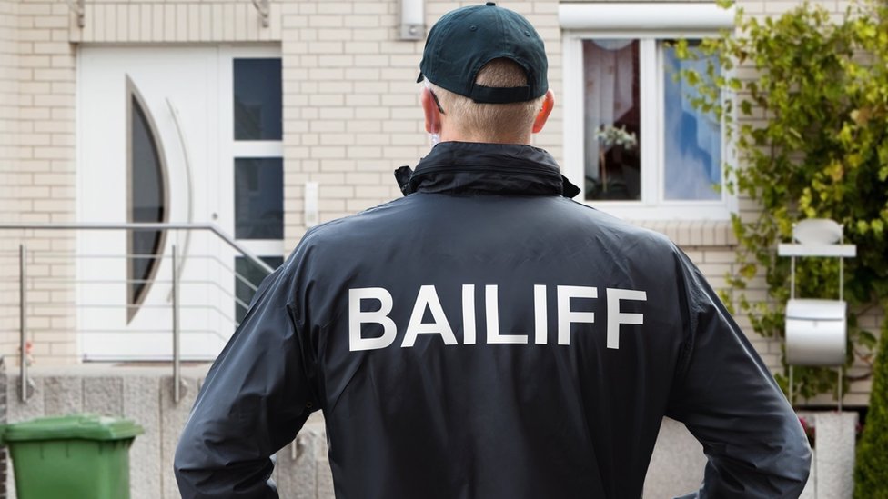 Bailiff stands in front of house
