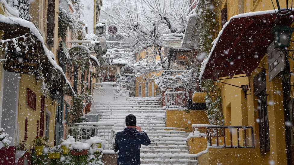 A man takes a photograph at the popular touristic area of Plaka during a heavy snowfall in Athens