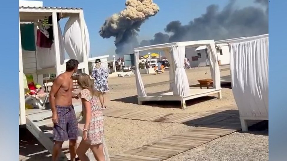 People on beach in Crimea, plume of smoke in background