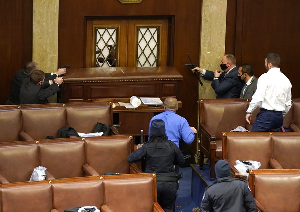 Capitol police officers point their guns at a door that was vandalized in the House Chamber during a joint session of Congress on 6 January 2021 in Washington, DC.