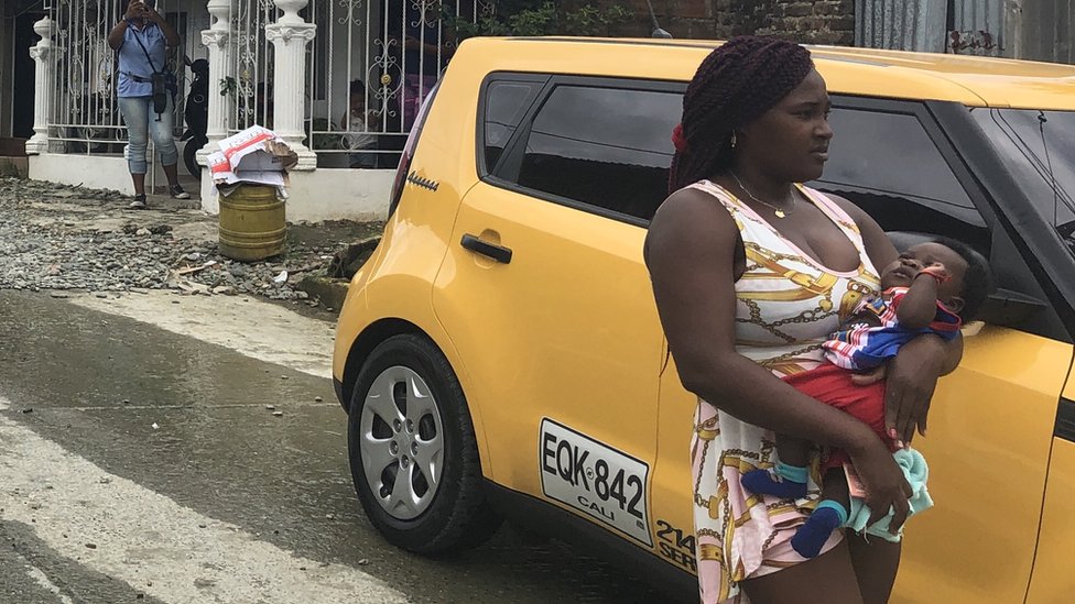 Una mujer con un niño en brazos al lado de un auto amarillo