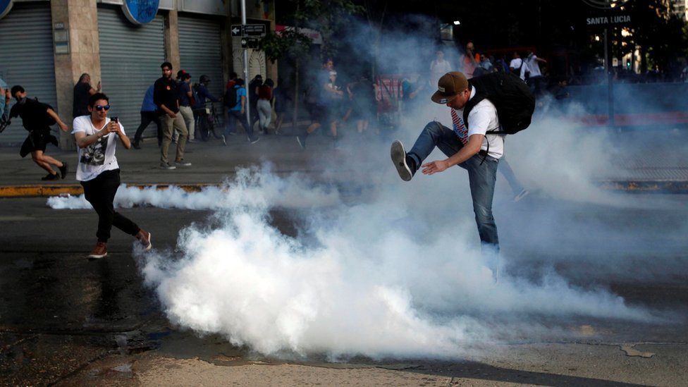 Демонстрант пинает баллончик со слезоточивым газом во время акции протеста против повышения цен на билеты в метро в Сантьяго