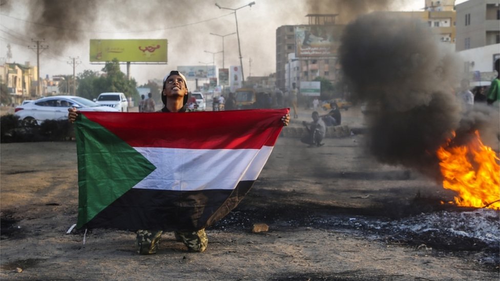 متظاهر سوداني يحمل العلم الوطني بجانب الإطارات المحترقة خلال مظاهرة في العاصمة الخرطوم، السودان، 26 أكتوبر/تشرين الأول 2021