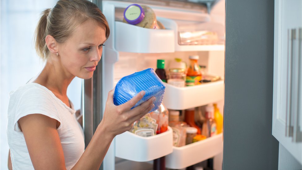 Una mujer mira un producto que saca del refrigerador.