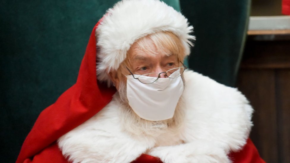 Santa Claus sits in a big chair while wearing a face mask at the Berkshire Mall Center court in Wyomissing