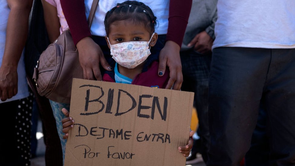 Criança pede em placa que Biden a deixe entrar nos EUA, em um protesto de migrantes na fronteira do México com a Califórnia