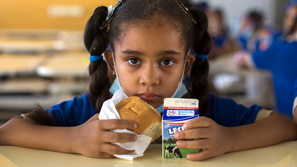 Niña en una escuela con una porción de leche y un pan