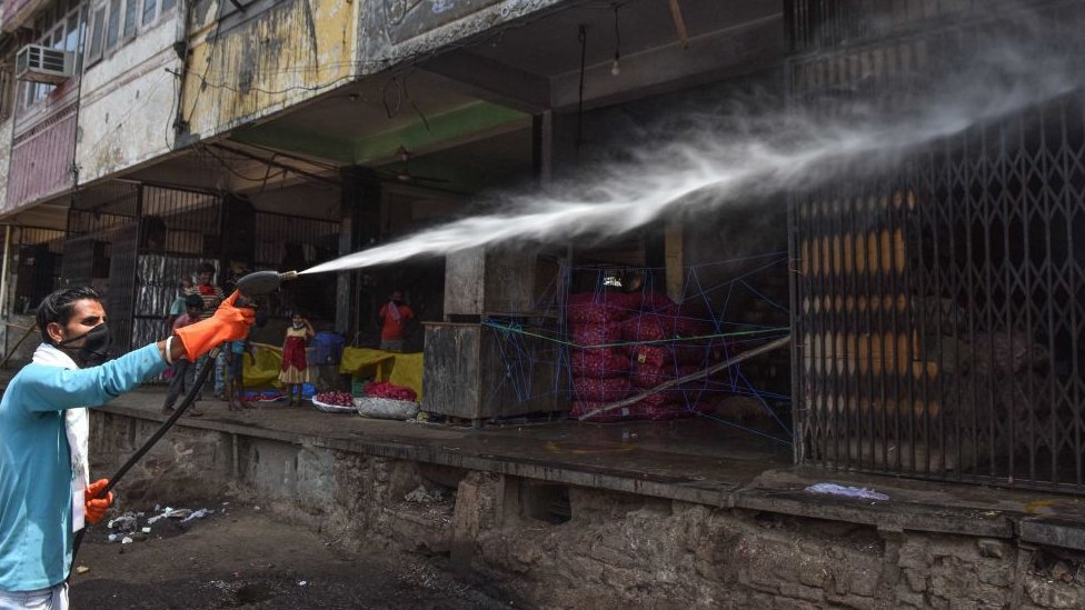 Санитарный работник распыляет дезинфицирующее средство над магазинами в Азадпур Манди, 1 мая 2020 года в Нью-Дели, Индия.
