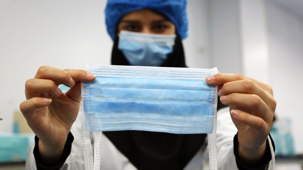 Женщина держит медицинскую маску на фабрике, которая работает круглосуточно в Тегеране, Иран
