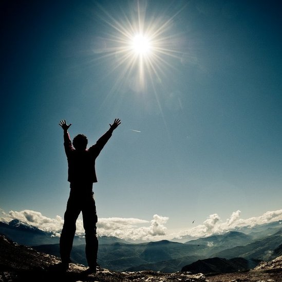 Un hombre en la cumbre de una montaña con los brazos en alto hacia el sol