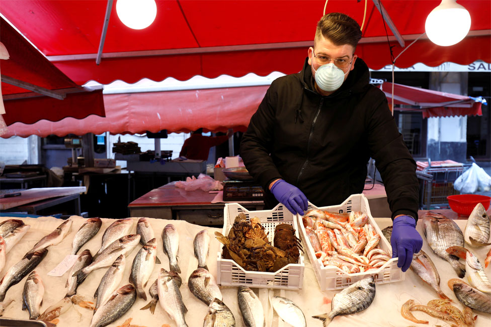 A man wearing a face mask next to a fish market stall