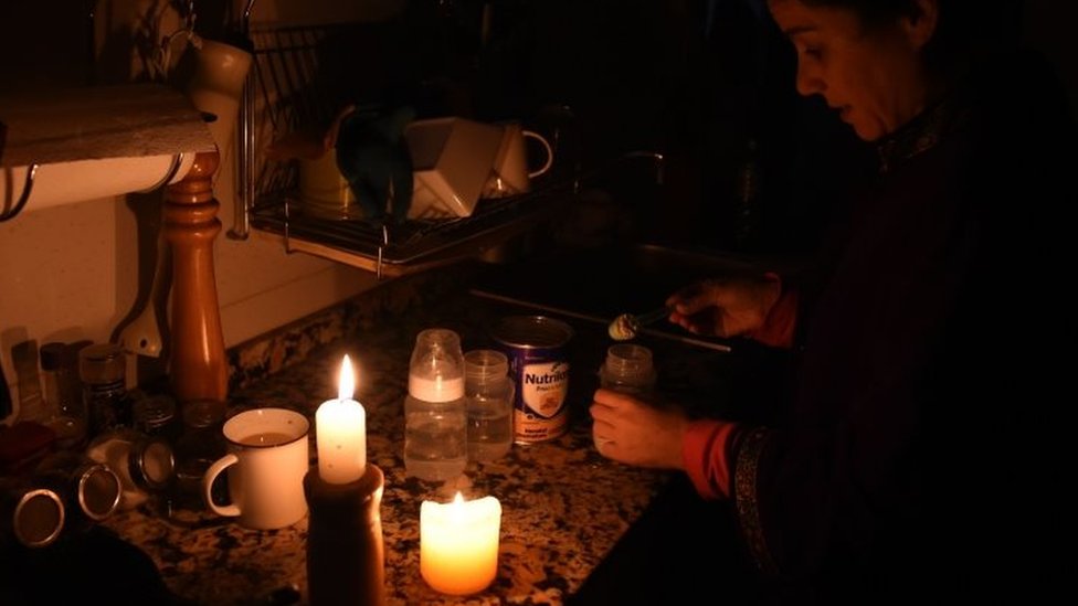 Женщина работает при свече на кухне во время отключения электроэнергии в Уругвае