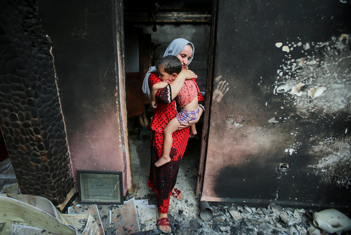 ​​A mother carries her child as she inspects the damage to her house by wildfires in Bejaia, Algeria - 25 July 2023