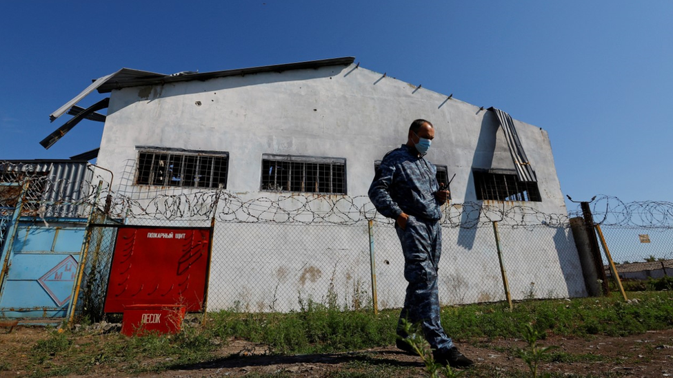 A security guard stands outside one of the white prison buildings surrounded by barbed wire in Olenivka